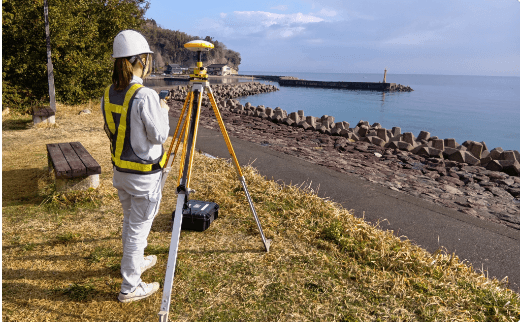 海岸沿いでGNSS測量機器を使い高精度な基準点測量を行う作業員